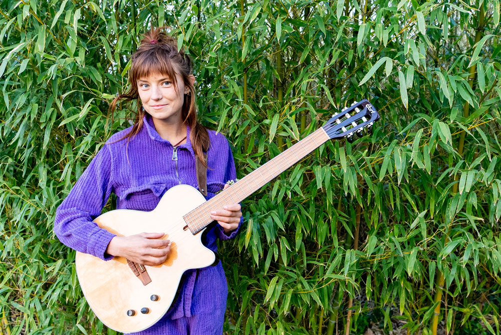 Chloe Levaillant lady playing guitar in front of hedge